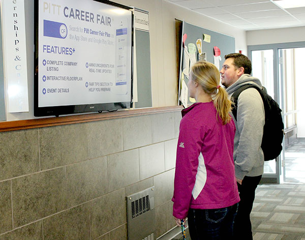 Freshman Alaina Thomas (left) and junior Gino Szegedy (right) read internship and career information displayed on the televsion located in Biddle Hall.