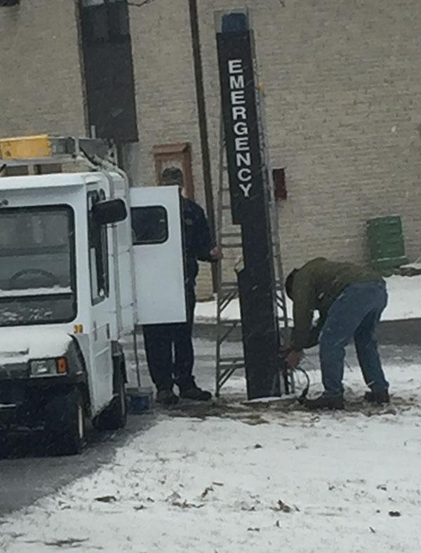 Two maintenance employees work around an emergency phone in between Summit and Highland Townhouses.