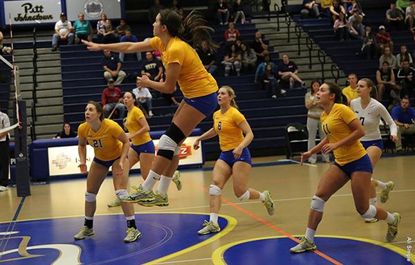 Pitt-Johnstown’s red shirt junior outside-hitter Marissa Erminio in the air with a spike as teammates watch the play develop.