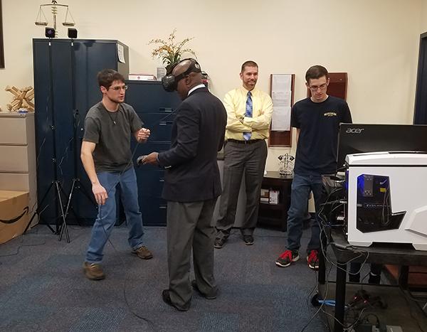 Senior Thomas Plutt helps President Jem Spectar with the new virtual-reality equiptment to be set up in the Zone. Sophomore Nick Marconi (right) and Student Affairs Vice President Shawn Brooks (second from right) monitor Spectar’s experience on a computer. 