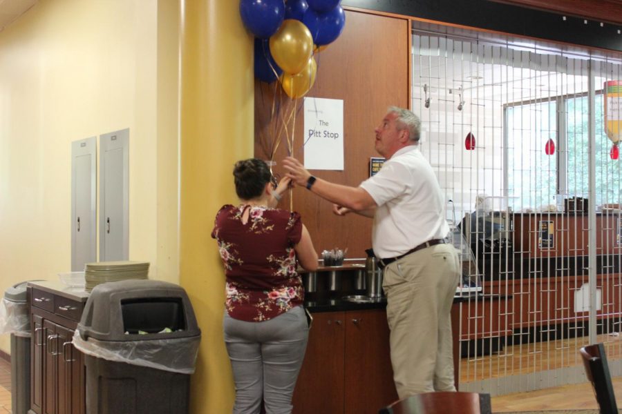 Sodexo Unit Marketing Coordinator Emily Cairns (left) and Dining Services Director Bob Knipple (right) arrange balloons next to a sign announcing the new café’s name, the Pitt Stop.